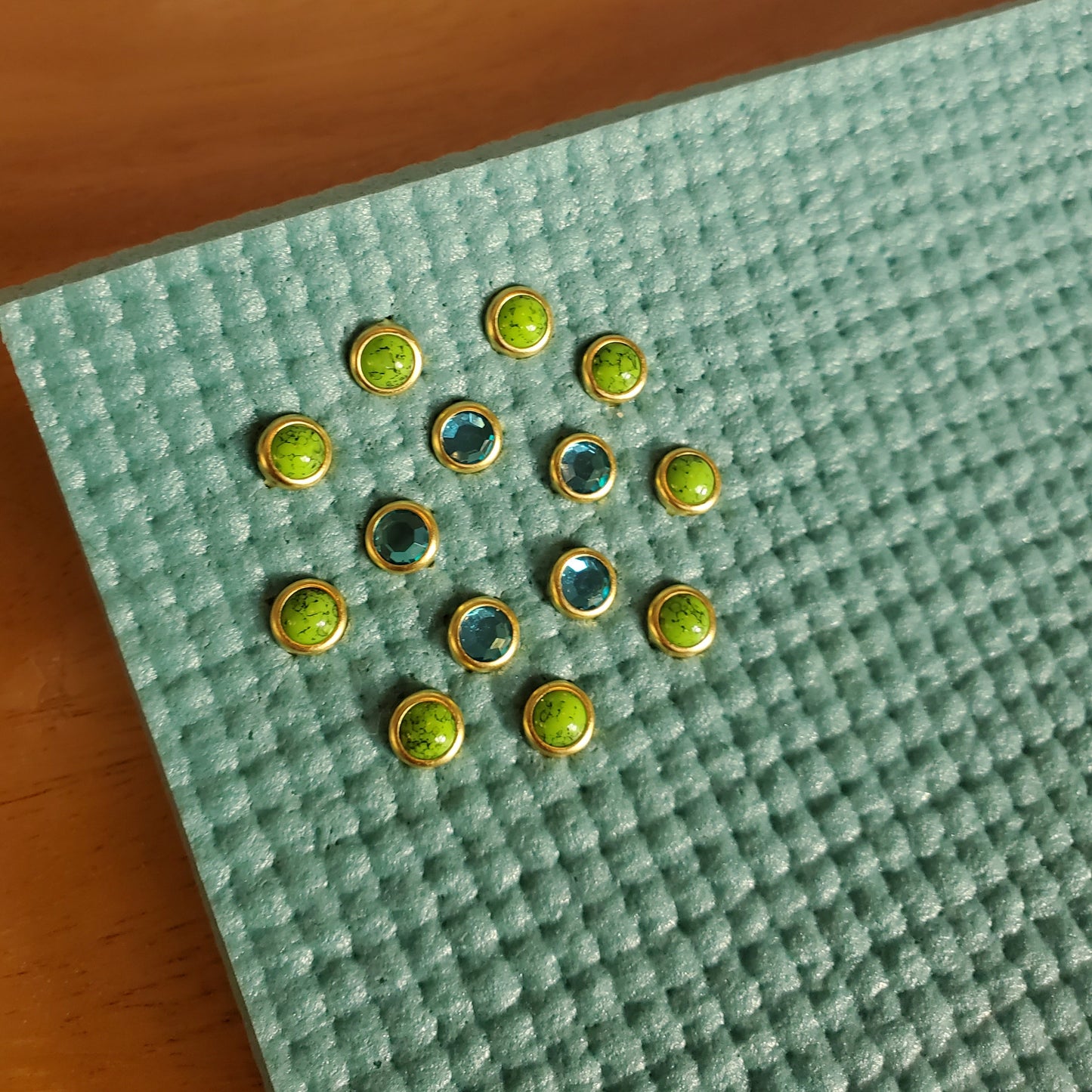 green stones and turqouise gems set in gold installed in a light blue yoga mat
