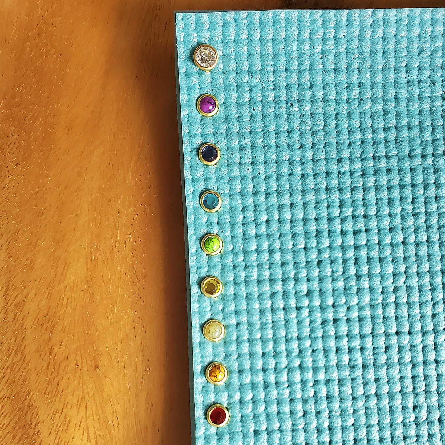 Turquoise yoga mat with chakra yoga mat charms on a wooden floor
