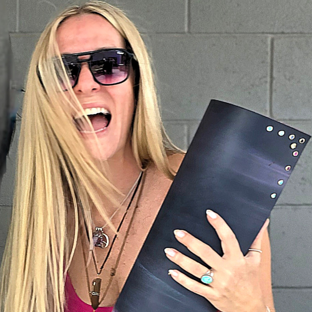 Woman holding a yoga mat with decorative yoga mat charms installed. She is against a gray wall.