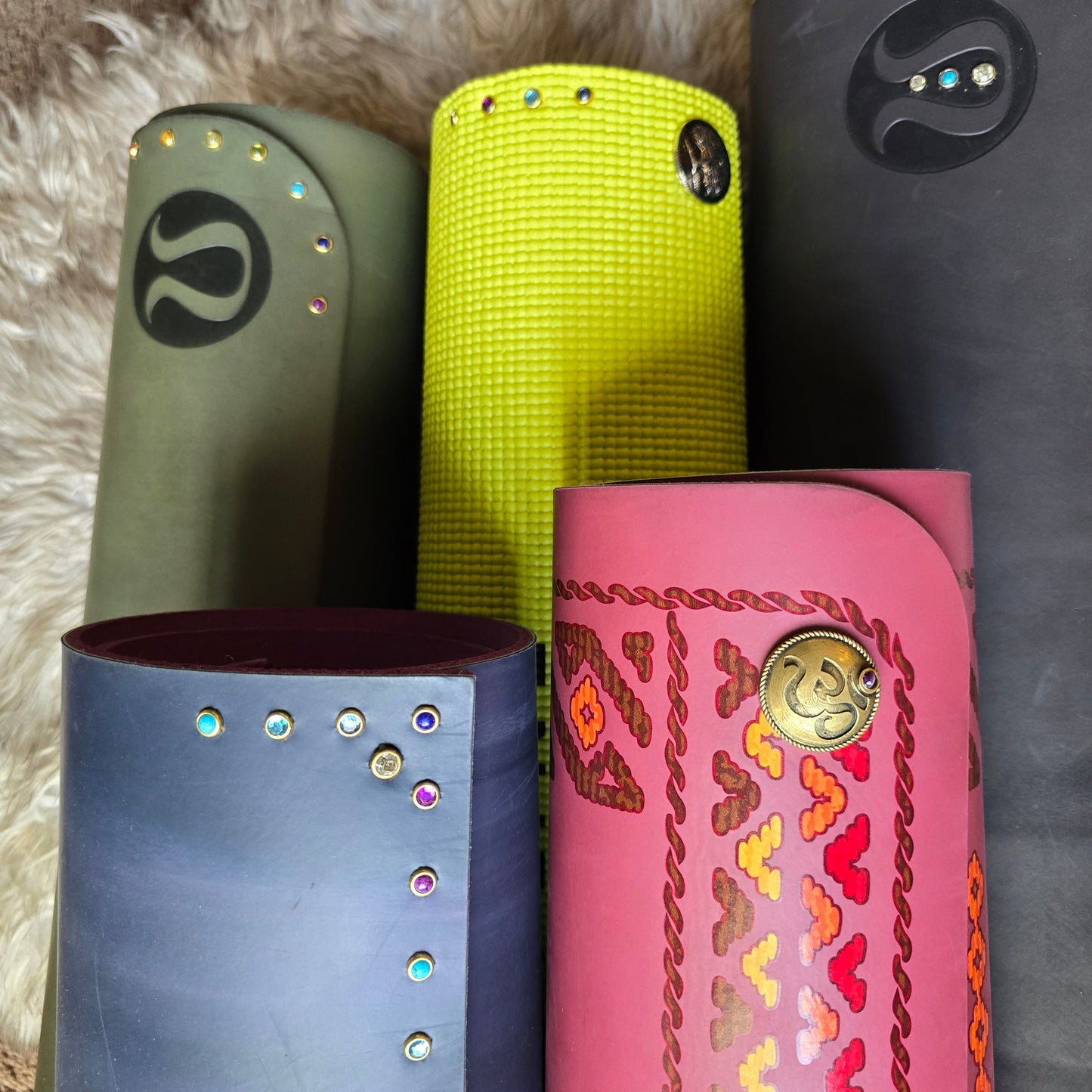 Stack of colorful yoga mats rolled-up all adorned with yoga mat charms in different designs